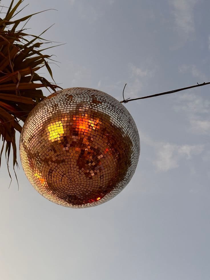 Disco ball reflecting warm light against a pale sky