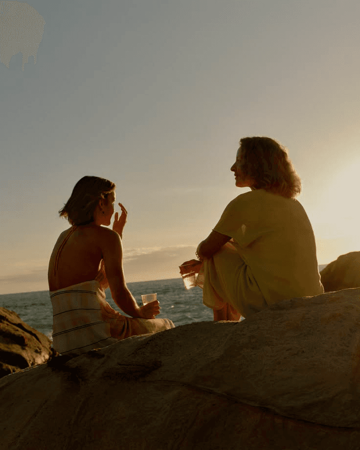 Two people in conversation on coastal rocks at golden hour